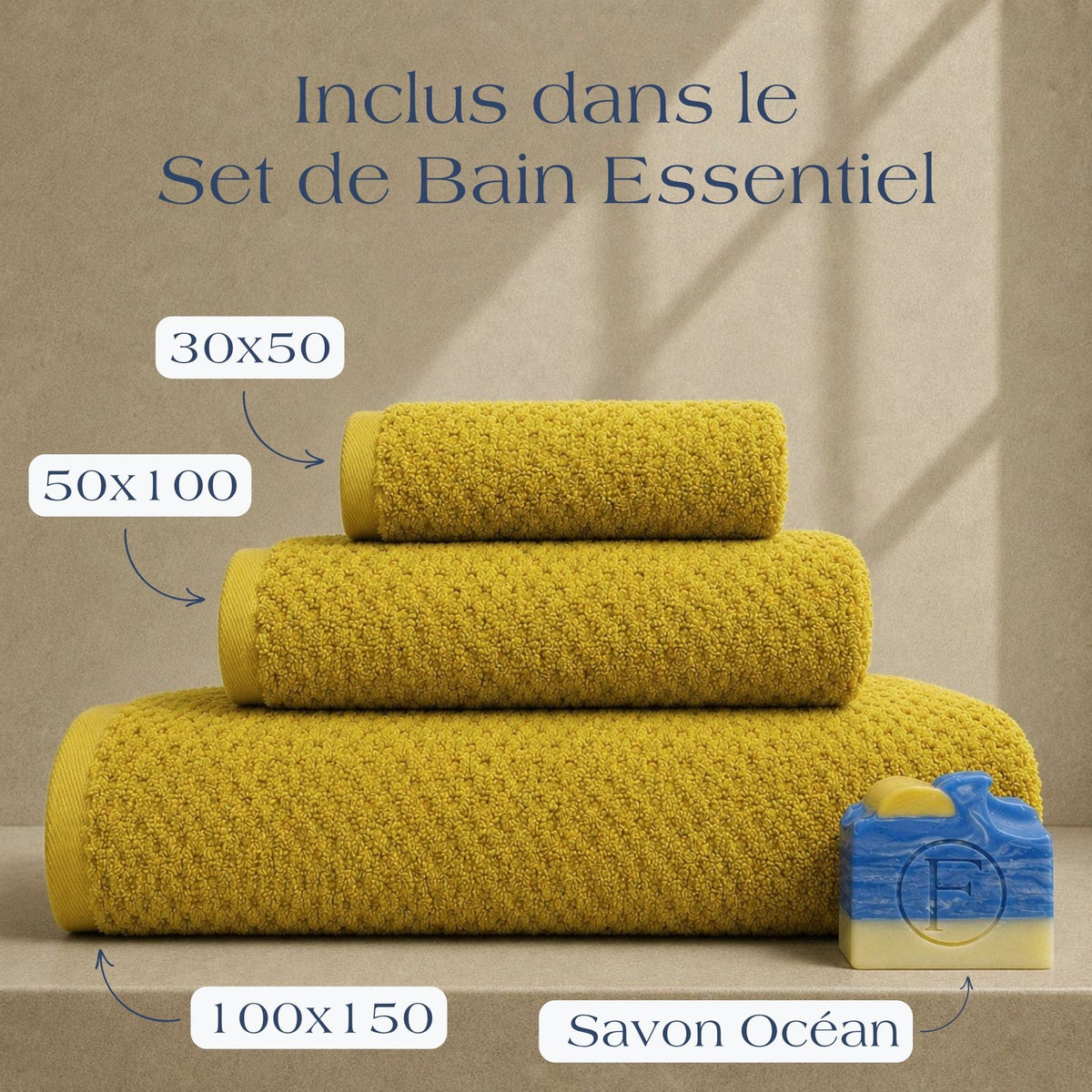 Set de Bain Essentiel FLAMARDA Prestige Dune Ocre Doré comprenant un drap de bain 100x150cm, une serviette 50x100cm, une serviette invité 30x50cm et un savon artisanal Océan, présenté dans une ambiance lumineuse aux accents solaires.