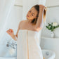 Femme en sortie de bain, enveloppée dans un drap de bain couleur sable naturel FLAMARDA. Linge de bain haut de gamme aux tons doux, inspiré des plages portugaises et du luxe quotidien.