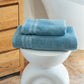 Serviettes de bain FLAMARDA bleu horizon pliées avec soin sur un tabouret sculptural blanc, dans une salle de bain élégante. Linge de bain haut de gamme à l’inspiration marine, alliant qualité, douceur et design raffiné.